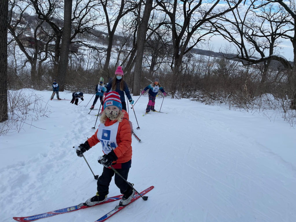 Child on cross country skis with more skiers behind them on the snowy trail